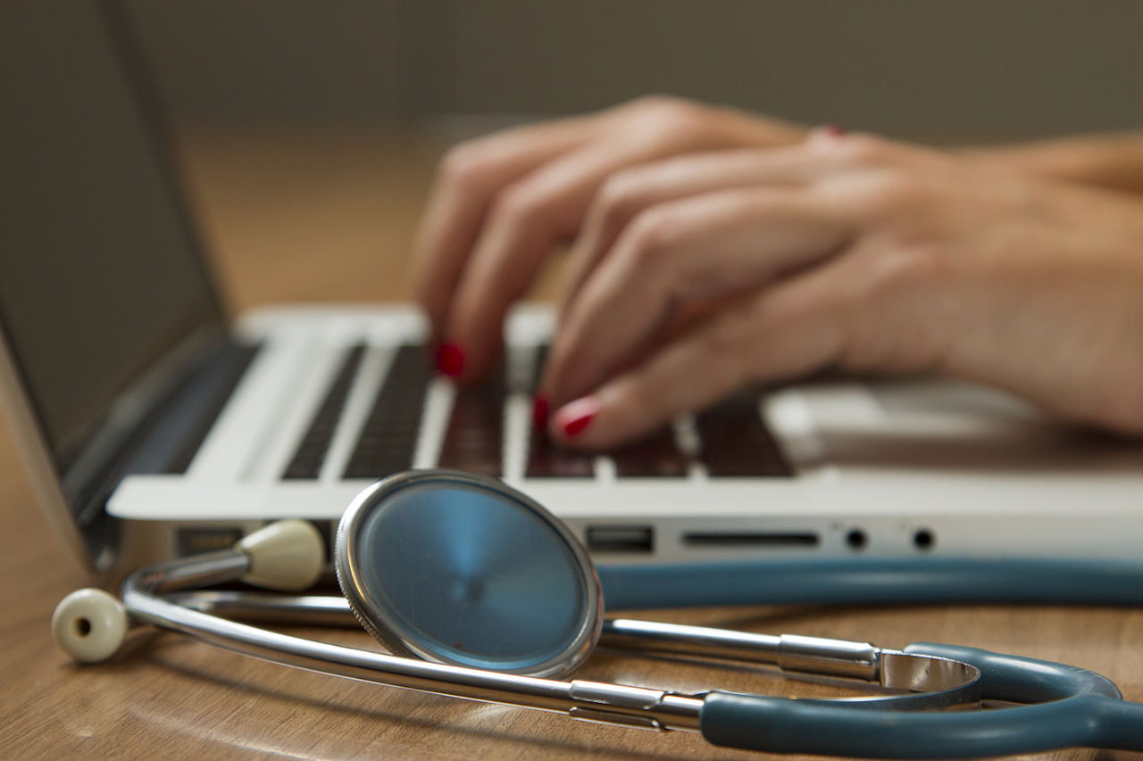 Stethoscope resting on a laptop while a clinician types—tech assisting care